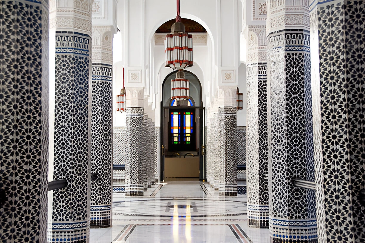 Interior of a Moroccan mosque with zellige columns, white arches and hanging lanterns