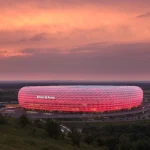 Vue de l’Allianz Arena à Munich illuminée en rouge au coucher du soleil.