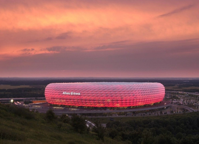 Vue de l’Allianz Arena à Munich illuminée en rouge au coucher du soleil.