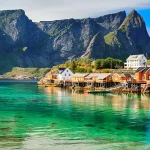 Maisons colorées sur pilotis au bord d’un fjord avec montagnes en arrière-plan, proposées par 2S Africa Travel, agence de voyages à Rabat