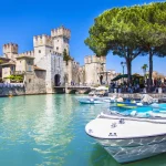 Vue du lac de Garde à Sirmione avec le château médiéval, des bateaux et des eaux turquoise.