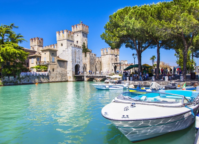 Vue du lac de Garde à Sirmione avec le château médiéval, des bateaux et des eaux turquoise.