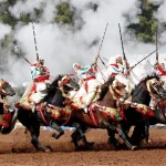 Fantasia marocaine avec cavaliers en tenue traditionnelle tirant à la poudre noire lors d’un spectacle équestre.