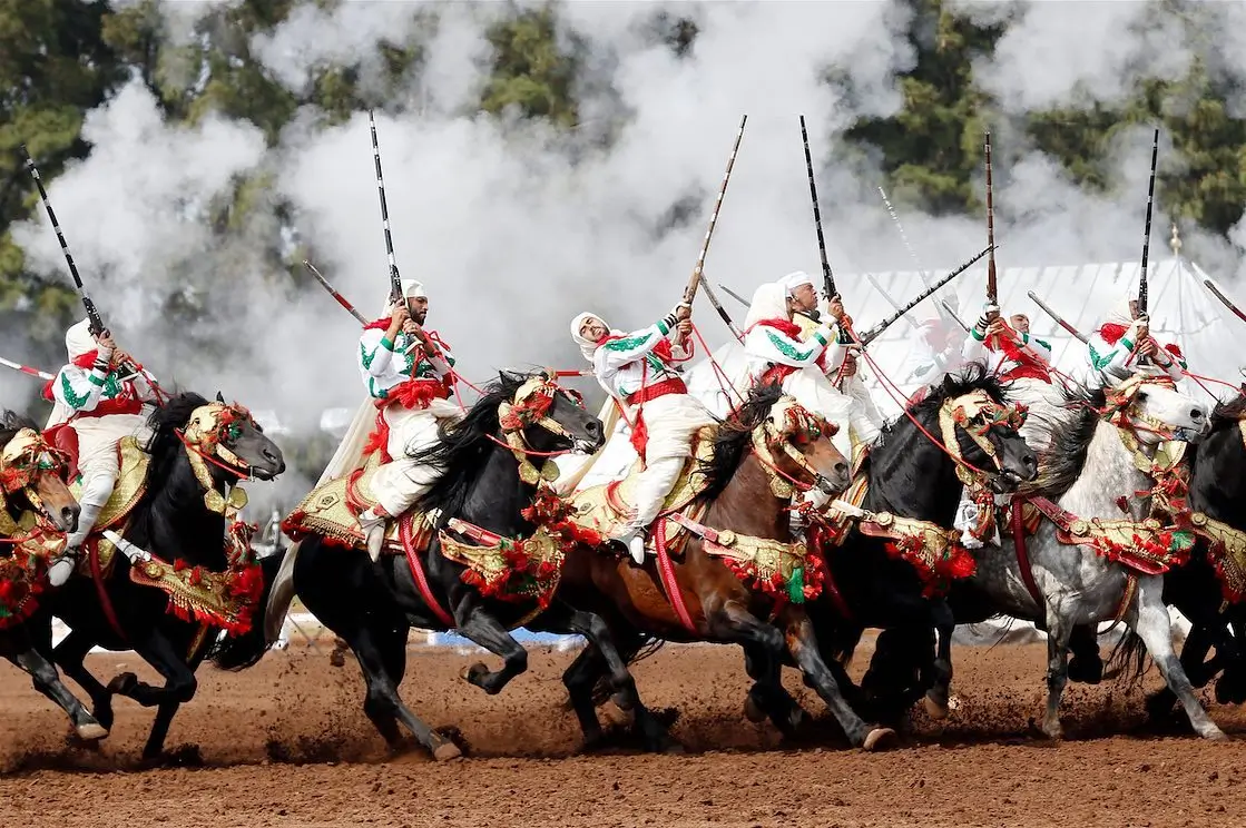 Fantasia marocaine avec cavaliers en tenue traditionnelle tirant à la poudre noire lors d’un spectacle équestre.